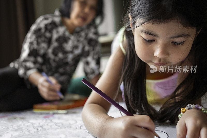 一个小女孩在家里和她的奶奶一起给图画上色