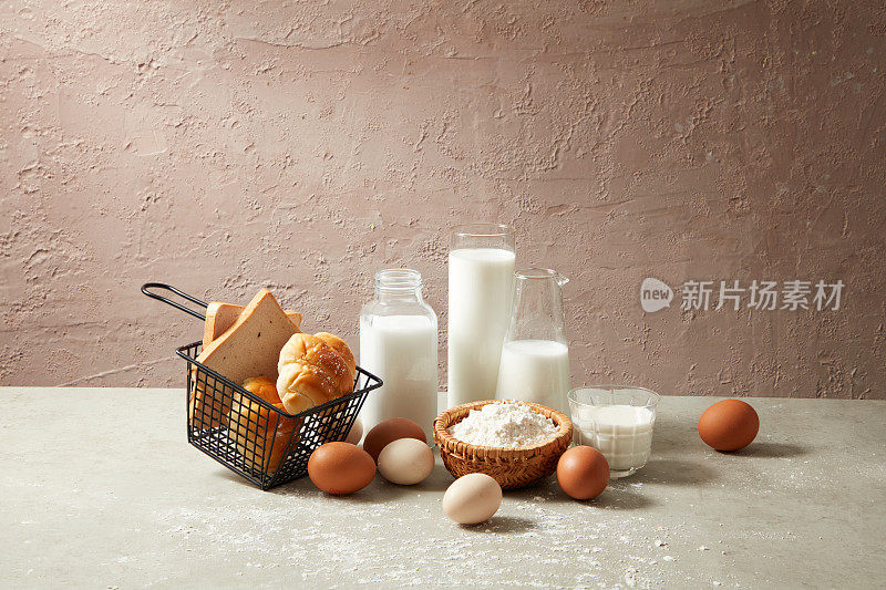 正视图的烘焙材料装饰着新鲜的牛奶，鸡蛋，面粉，一些三明治和羊角面包在水泥背景和灰色的厨房桌子。用于展示产品的复制空间和空白空间