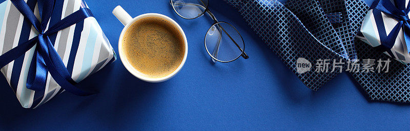 庆祝的早晨:一个充满活力的蓝色工作空间的俯视图，上面有一个包装整齐的礼物，蓝丝带，领带，一杯热咖啡，时尚的眼镜，等等。完美的父亲节生日主题