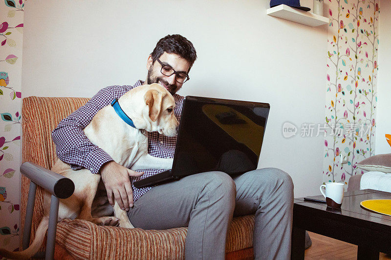 一个人在家里用笔记本电脑工作，他的宠物狗就在他旁边