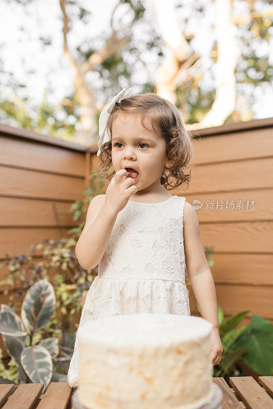 在新冠肺炎期间，小女孩在家的2岁生日派对上尝试她的简单奶油生日蛋糕