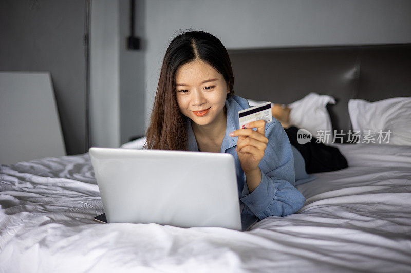 年轻女性躺在床上用笔记本电脑网购