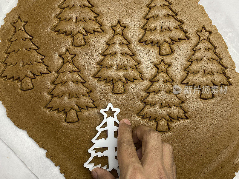 特写画面:一个不认识的人正在用塑料圣诞树饼干刀切自制的饼干，姜饼曲奇面团滚在防油的羊皮纸上，树被切出形状，家庭烘焙，高架视野