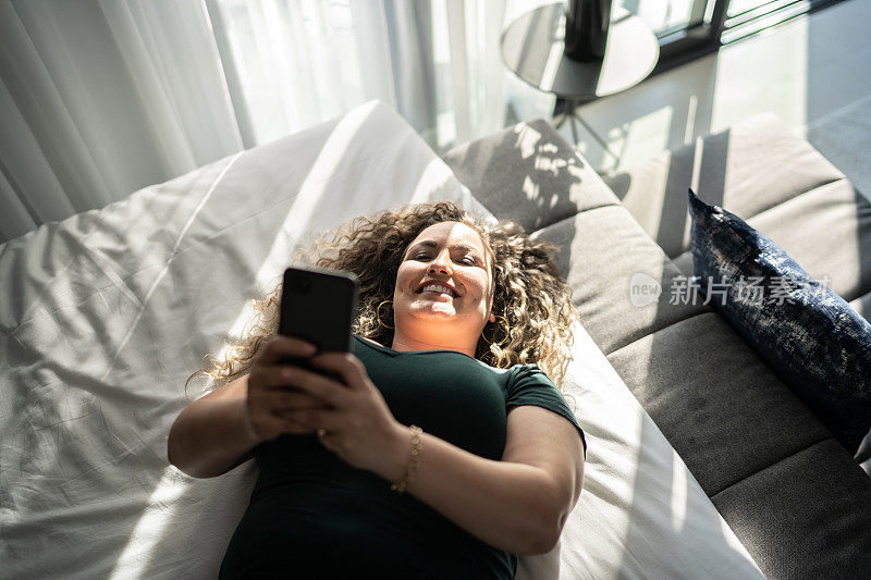 女人躺在家里的床上玩智能手机
