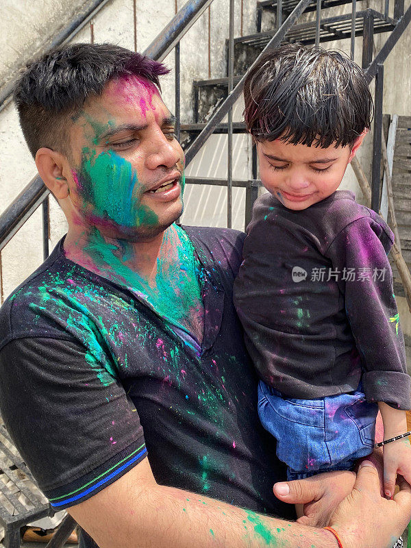 图为一名印度男子抱着年幼的女儿，身上涂满了油漆粉颜色的乌拉尔响，在胡里节的色彩和爱漆大战中胡闹