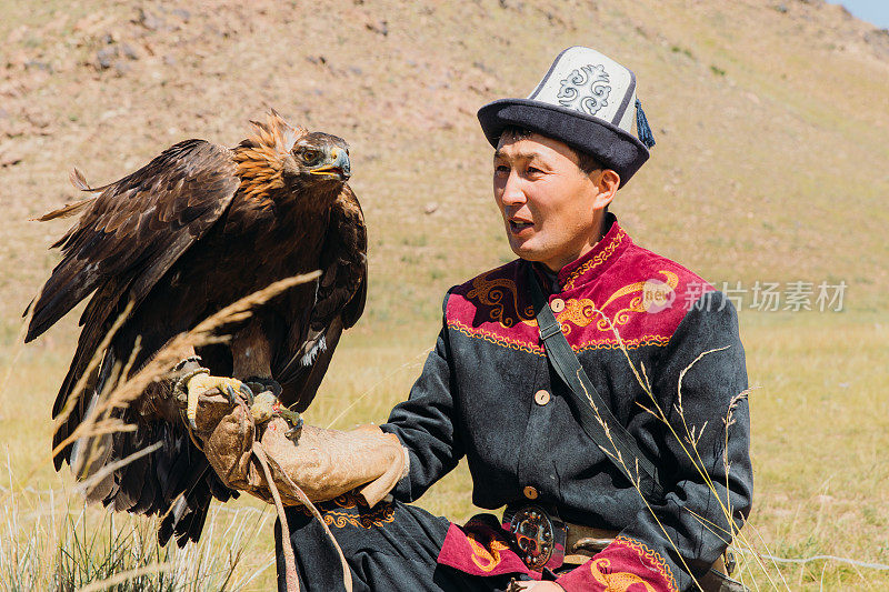 在中亚山区，身穿传统服装的老鹰猎人和老鹰在一起