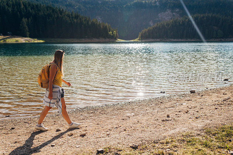 一个游客在湖边散步，享受着湖和周围森林的景色。