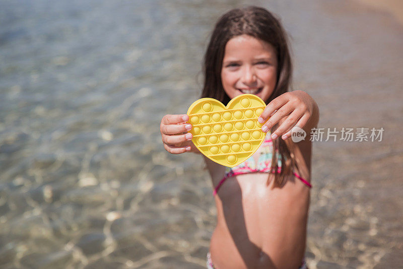快乐的女孩站在沙滩上，抱着心形的推大众的烦躁的玩具