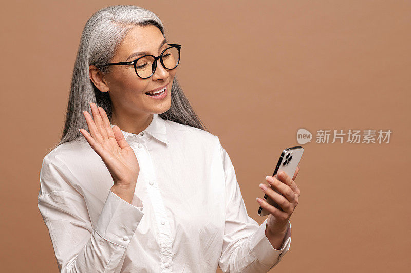 悠然成熟的白发老太太有喜虚拟会，现代奶奶挥手致意。庆幸的是，高级女性正在使用智能手机隔离视频连接
