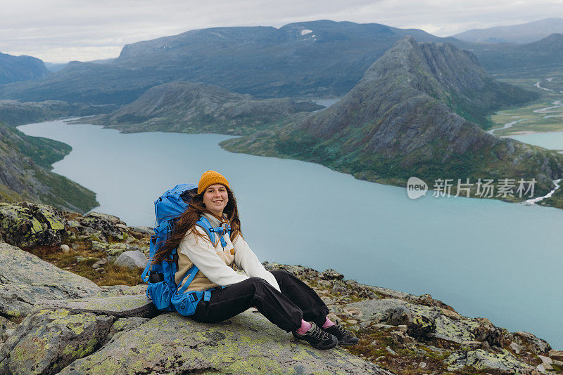 挪威约顿海门国家公园，一名女背包客坐在山顶上凝视着群山的侧视图