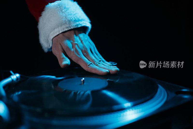 圣诞DJ在转盘上刮黑胶唱片。穿着红色圣诞服装的俱乐部磁盘小丑播放音乐