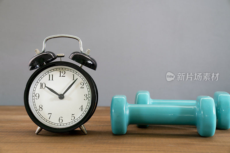 运动时间闹钟和哑铃，灰色背景，运动和健康的概念