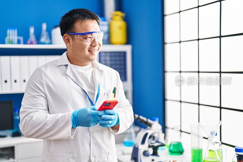 身着科学家制服的年轻中国男子在实验室使用智能手机