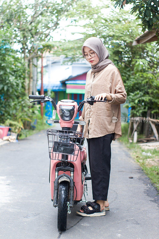 年轻的伊斯兰妇女在居民区骑电动自行车