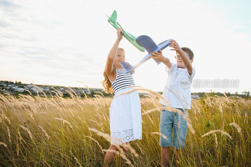奔跑的男孩和女孩拿着两个绿色和蓝色的飞机玩具在操场上在夏日阳光明媚的一天
