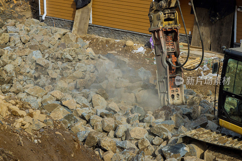 一台带有手提钻和液压锤的挖掘机正在用液压锤粉碎筑路用的大量石块