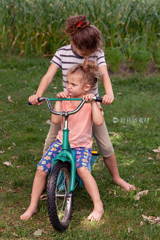 两个小女孩在公园里共用一辆自行车