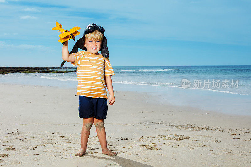 一个小男孩站在海滩上，拿着一个飞机玩具模型