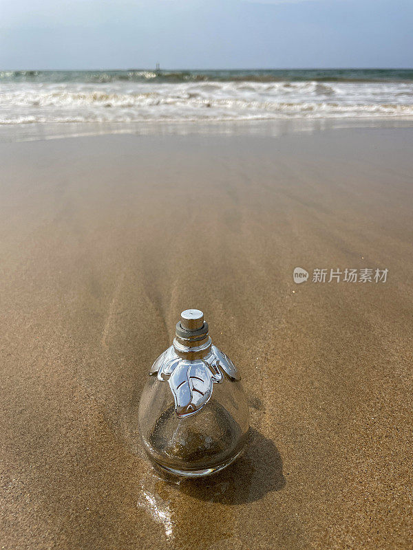 空的，玻璃香水瓶被冲到沙滩上的低潮水的边缘，破碎的海浪冲刷海洋垃圾和岸上的污染，乱扔的沙子，肮脏的海滩，关注前景，复制空间