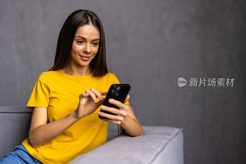 年轻漂亮的女人坐在客厅的沙发上，使用现代智能手机，在家打电话或订购。