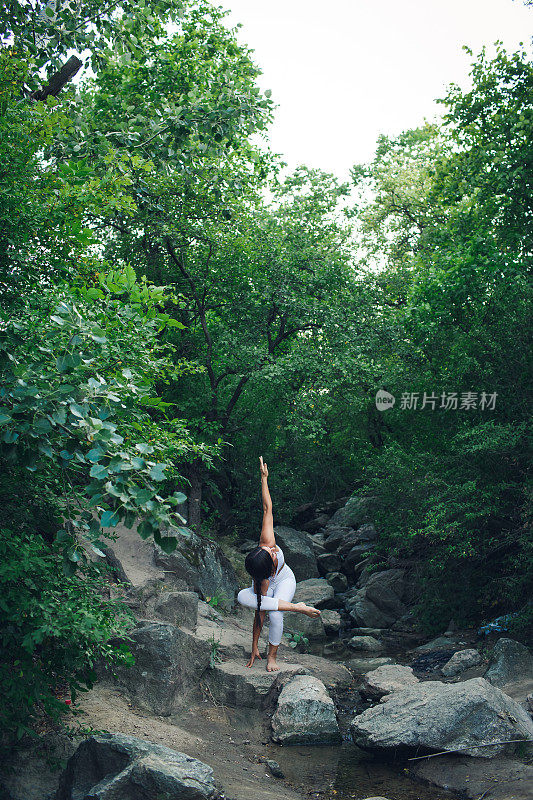 一个小女孩单腿站立做体式。一个女人在小溪边做瑜伽。