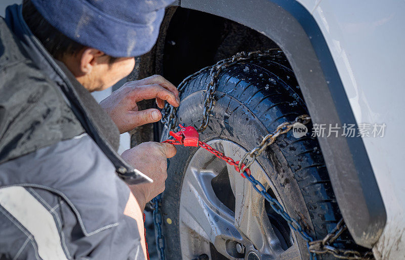 一名男子在他的车轮上安装雪链，以提高在冬季天气条件下的牵引力。