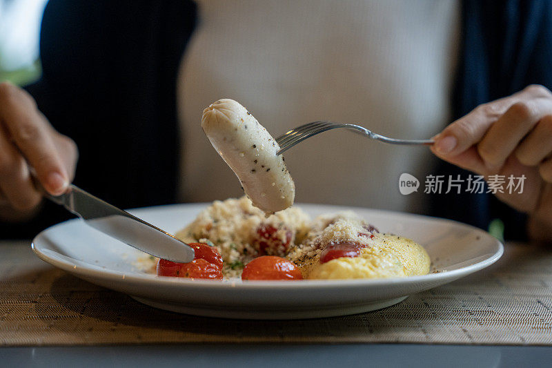 一名年轻女子坐在桌子旁，吃着早餐，有煎蛋、香肠和烤圣女果，为美好的一天奠定了基础