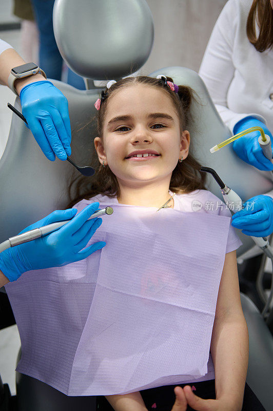 俯视图牙医和助手的手拿着无菌的牙科器械在一个微笑的小病人预约