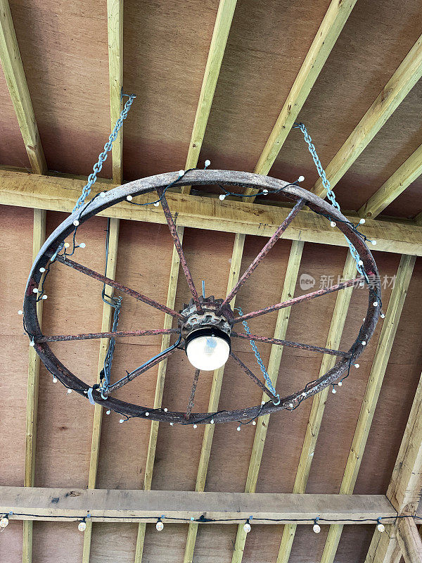 木梁谷仓天花板的特写图像与枝形吊灯，升级的照明设备，悬挂回收铁边马车车轮包裹着串灯，从下面看
