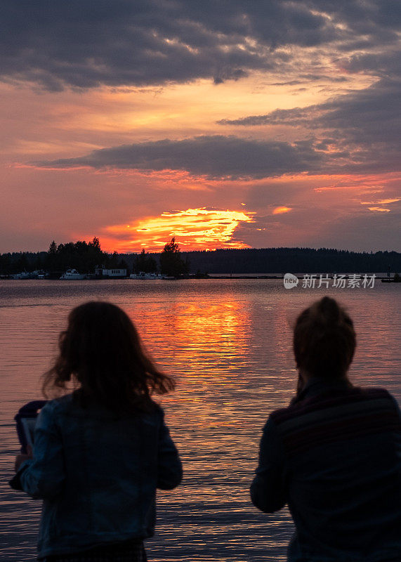 一个女孩，一个8岁的孩子，和一个年轻的女人在湖边看日落，用平板电脑拍照。