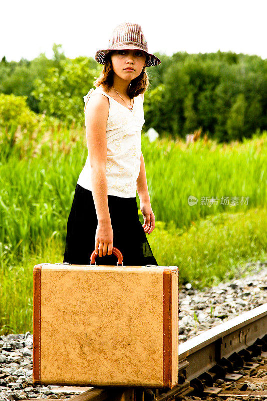 在铁路轨道上提着行李箱的年轻女孩注视着照相机