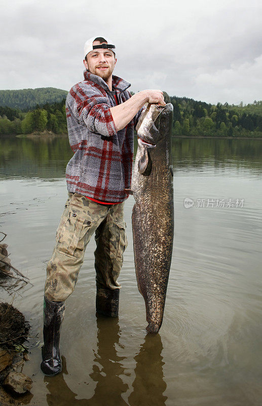一个渔夫在湖里抓着一条比他大一半的鲶鱼