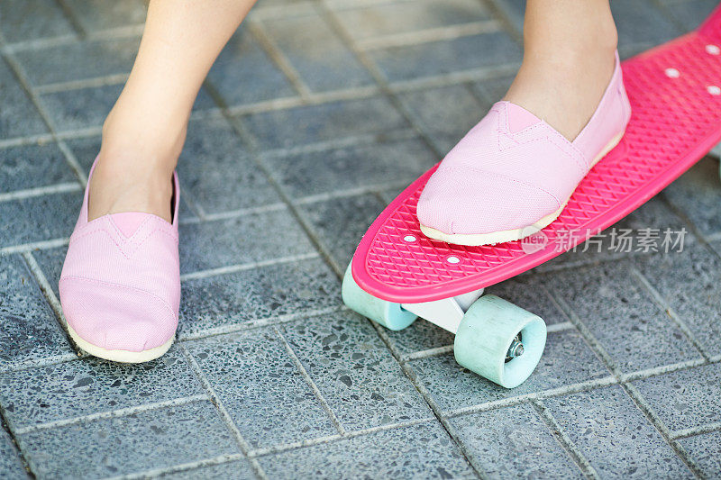 站在户外粉色滑板上的女孩。