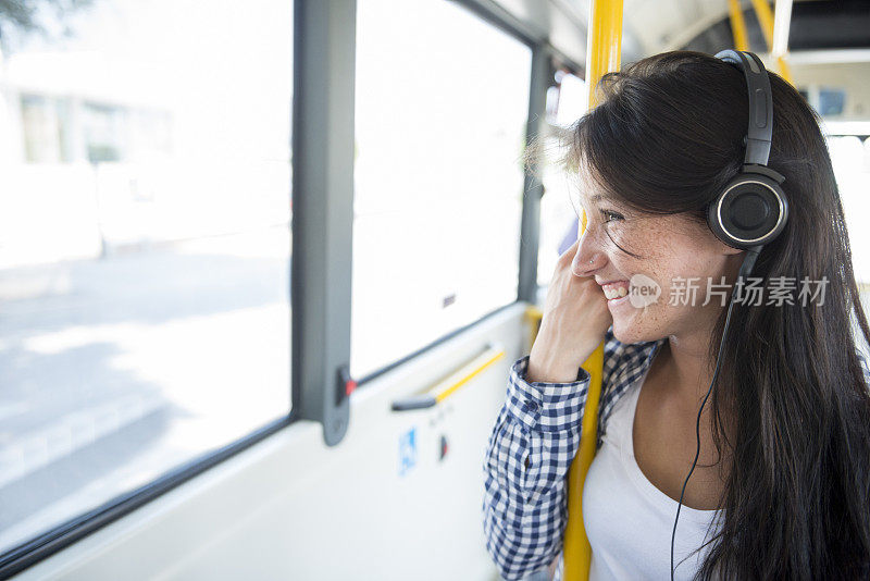 年轻快乐的女人在公共汽车上戴着耳机