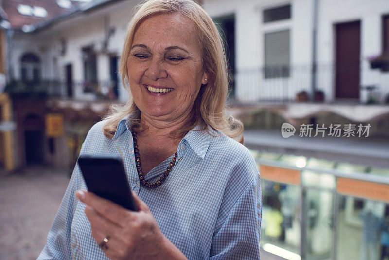 快乐的老妇人在户外用手机发短信。