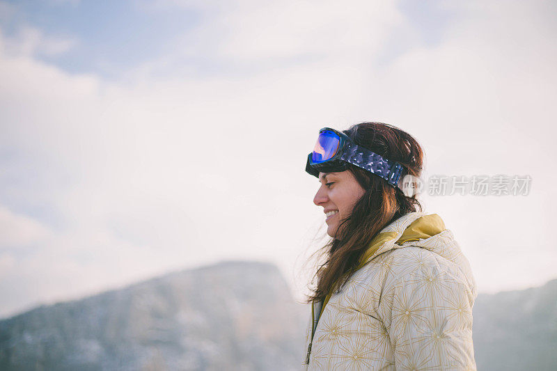 近景美丽的年轻女子在冬天的衣服站在一边，手拿木棍的背景雪山