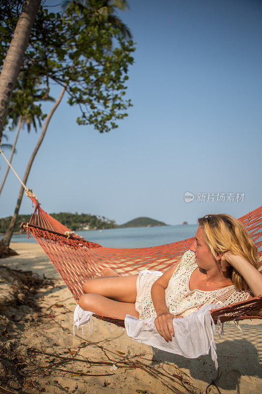 年轻女子躺在热带海滩的吊床上