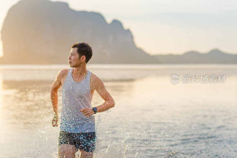 年轻的亚洲男子在海滩上奔跑，夕阳为背景