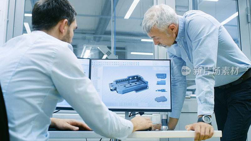工业设计人员在使用CAD程序，设计新部件时与高级工程师交谈。他从事双显示器个人电脑的研究。