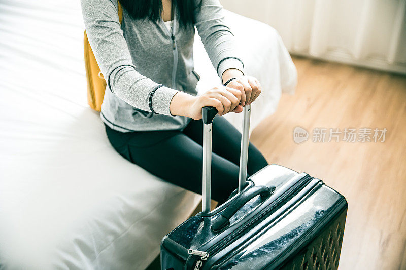 一个女人在旅馆里拿着行李坐在床上