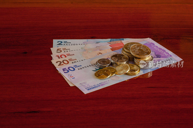 哥伦比亚，南美洲-获国际大奖的闪亮哥伦比亚硬币，放置在红木桌子上的新钞上。本空间
