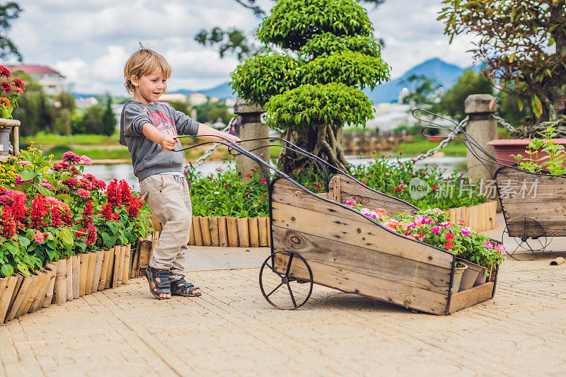 孩子推着手推车在花园里。可爱的蹒跚学步的小男孩在后院玩手推车。一个孩子在户外拖着玩具车