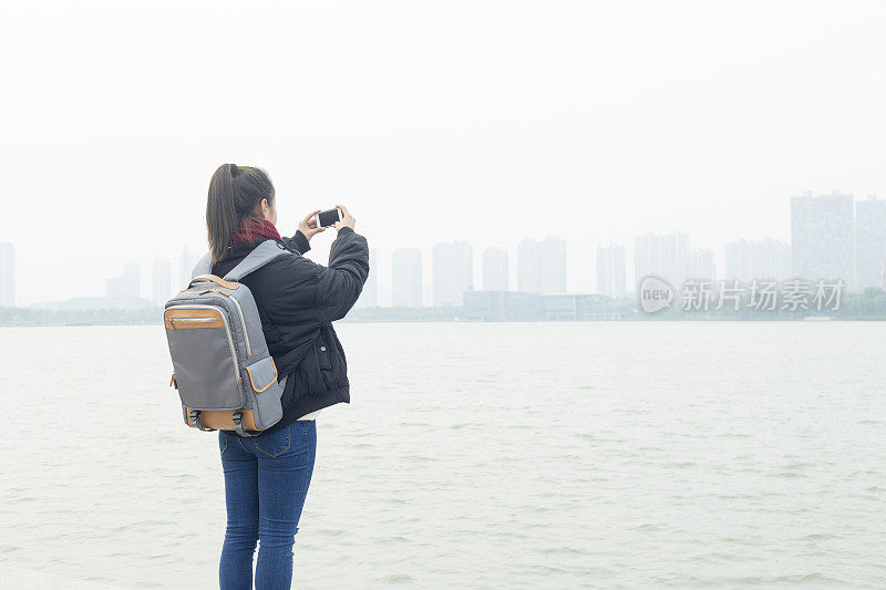 一个女人站在码头上用智能手机拍照