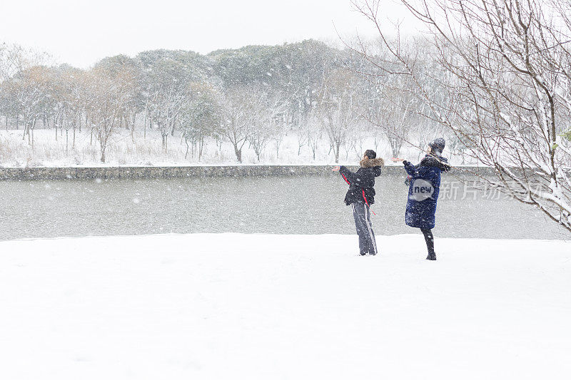 女性朋友穿着暖和的衣服在雪地里欢呼