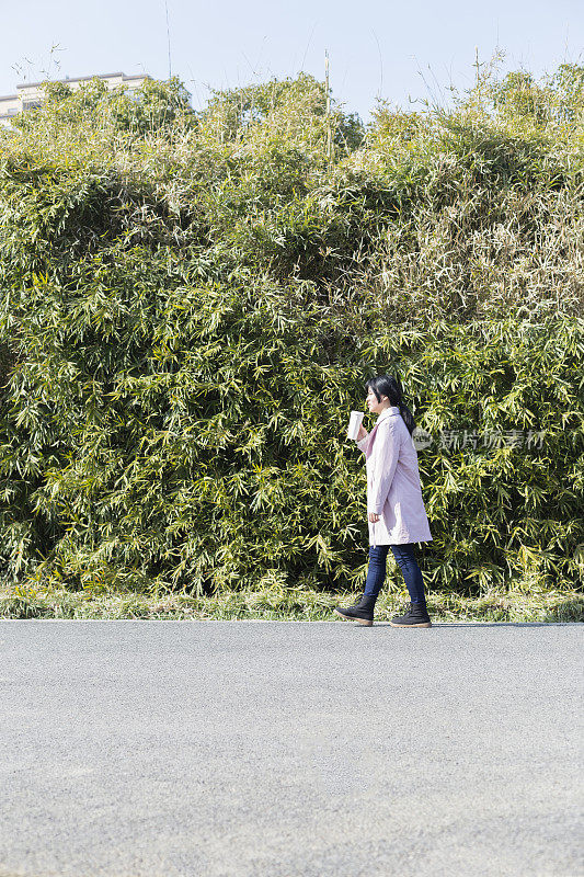 侧面的年轻女性拿着一次性杯子走在树上