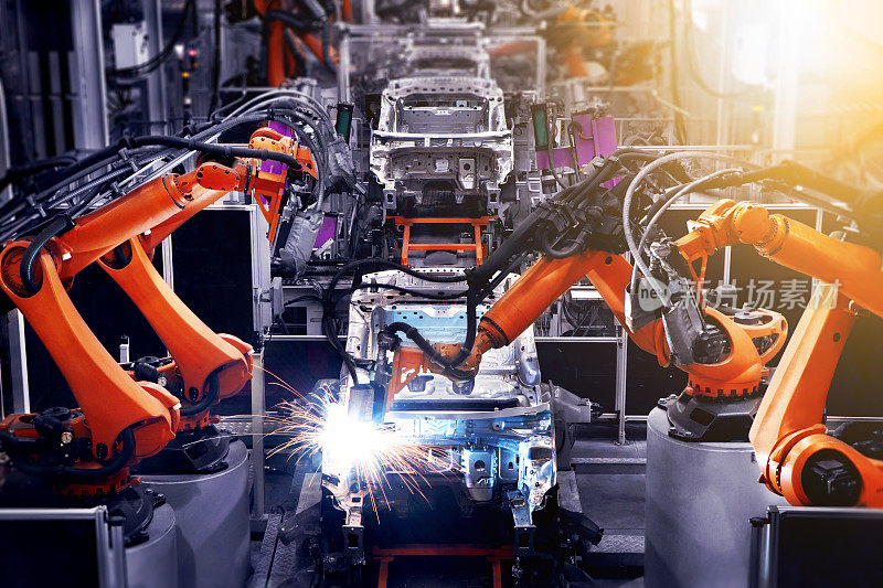 在工业生产车间，汽车生产线的机器人手臂正在工作