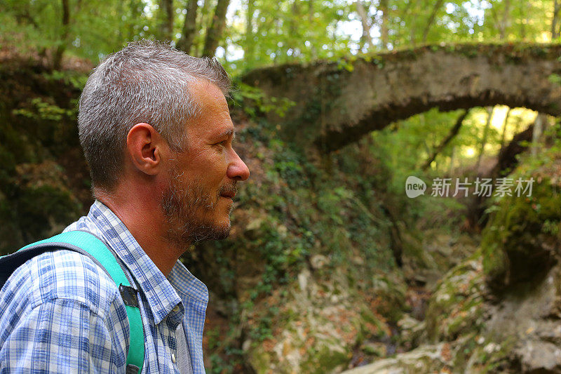 成年男子徒步旅行在美丽的自然景观与小溪流在森林和老废弃的石桥上面