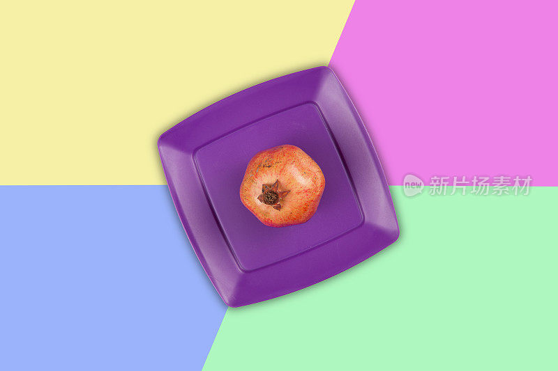 鲜红的石榴在紫色的塑料盘上，彩色的背景。
