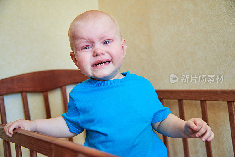 一个小男孩站在婴儿床上，哭着叫妈妈