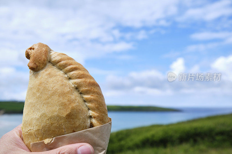 6月的一个阳光明媚的日子，手握康沃尔馅饼俯瞰纽基克兰托克海滩。
